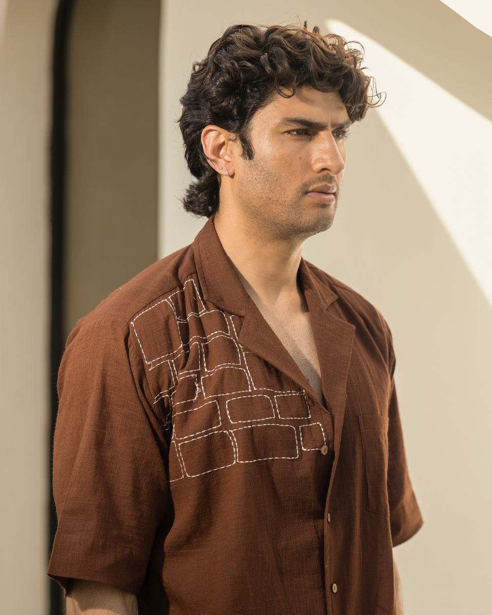 Man wearing a brown shirt with intricate patterns, standing against a neutral background