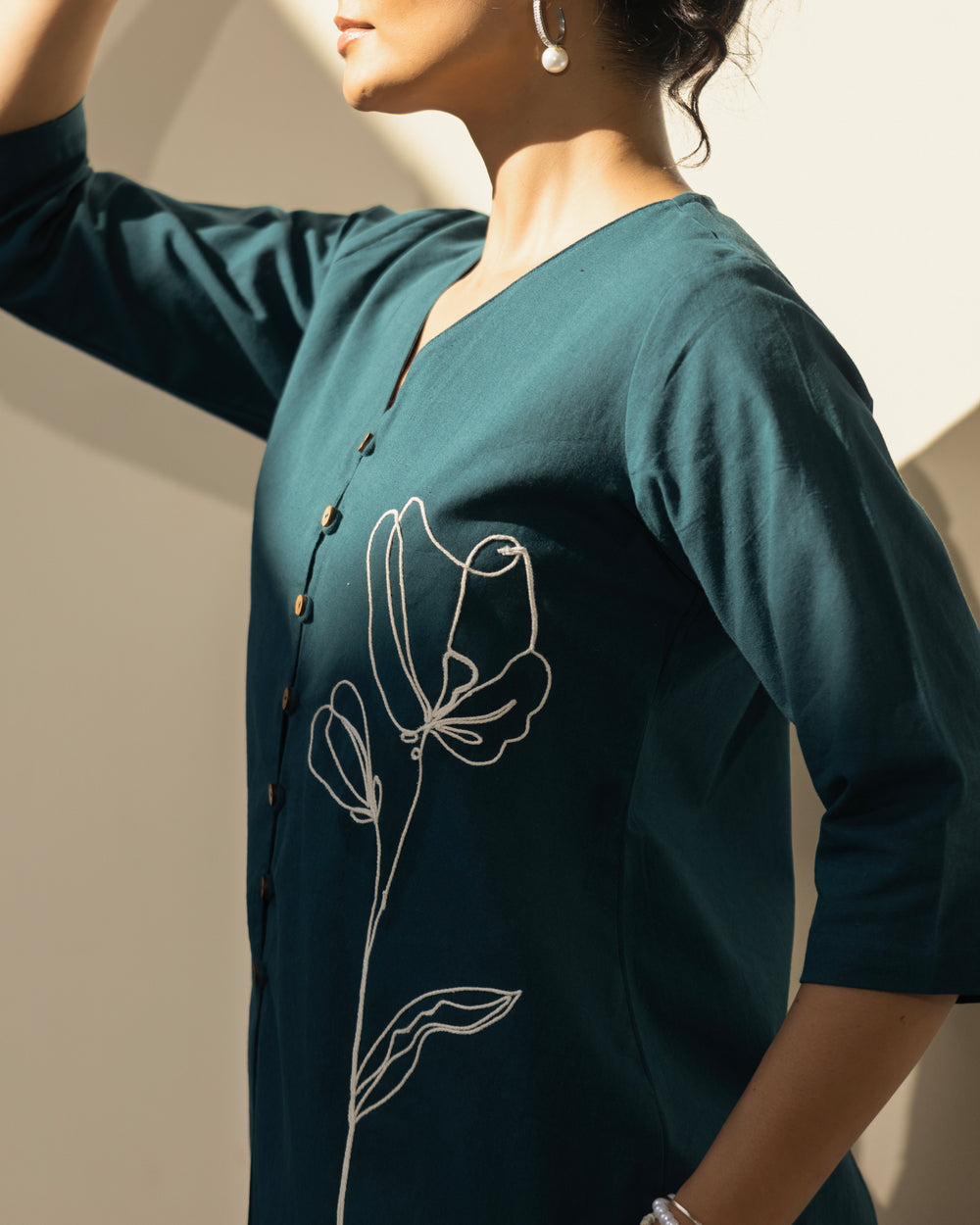 Woman wearing a teal dress with floral embroidery on a neutral background
