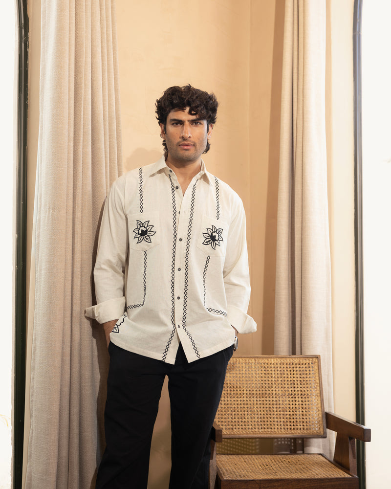 Man wearing a white embroidered shirt standing in front of beige curtains