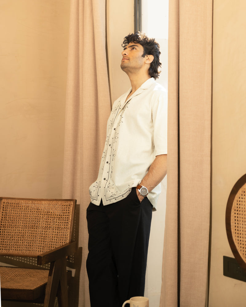 Man standing in a room with beige curtains and a chair.

