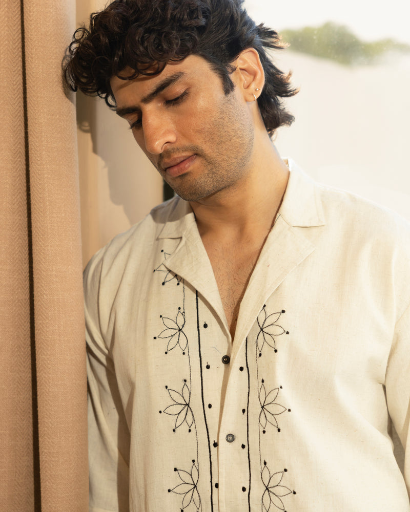 Man wearing a cream-colored embroidered shirt with black patterns.


