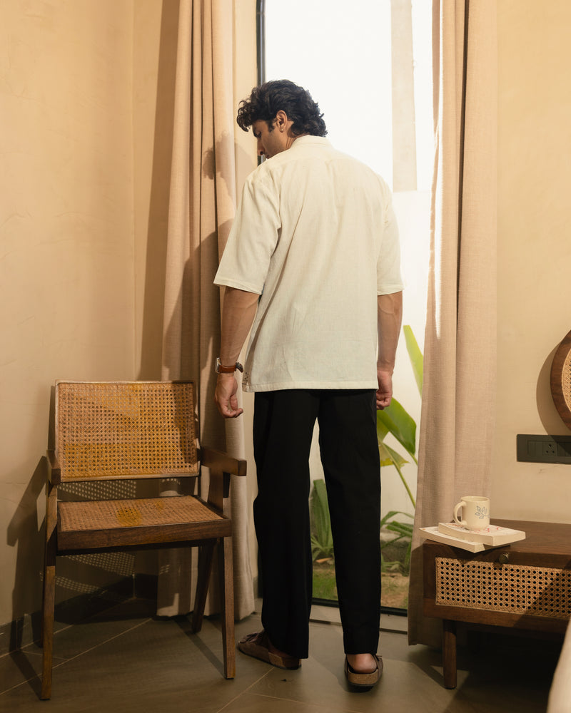 Man standing in a room with a chair and table, looking out a window.

