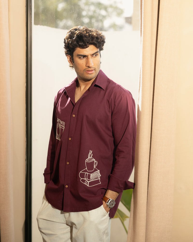 Man wearing a maroon shirt with a design, standing indoors.

