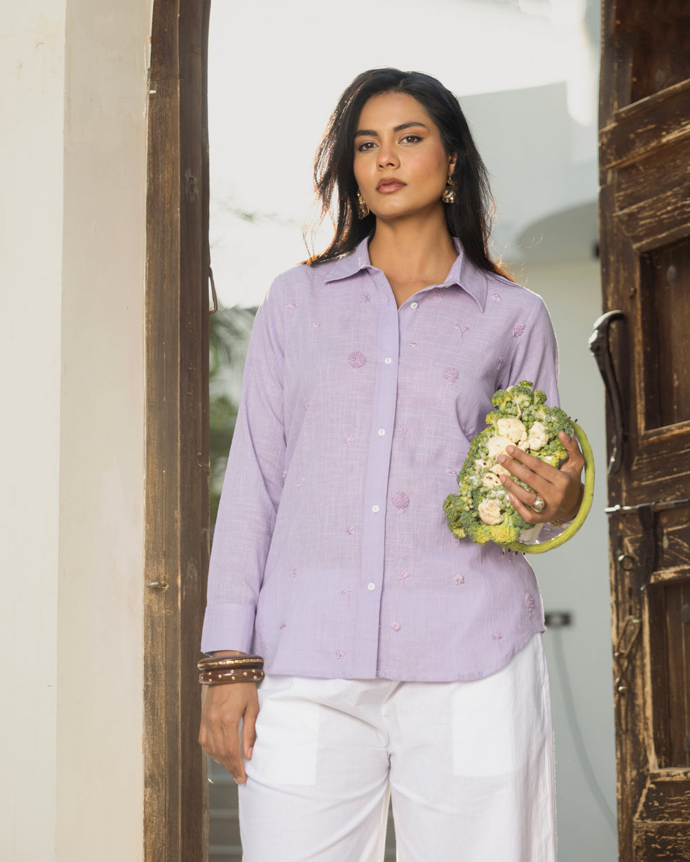 Woman in a light purple shirt holding a floral arrangement indoors.