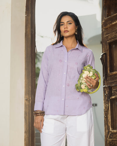 Woman in a light purple shirt holding a floral arrangement indoors.