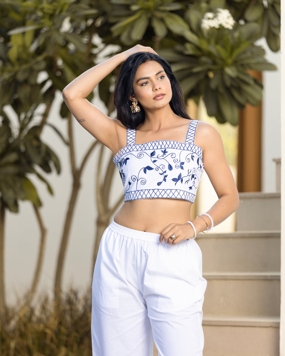 Woman wearing a white and blue patterned top with white pants outdoors.