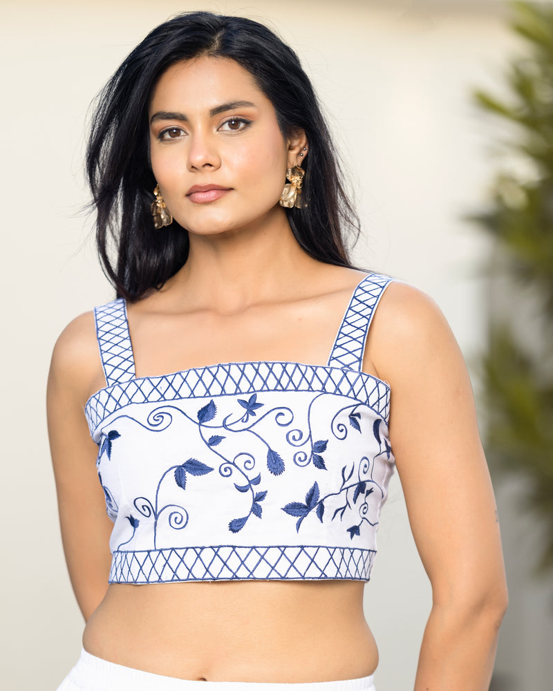 Woman wearing a blue and white embroidered top against a neutral background