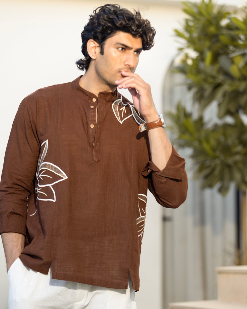 Man wearing a brown shirt with white patterns, standing indoors with a blurred background