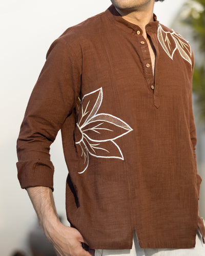 Brown shirt with white floral embroidery worn by a person against a neutral background