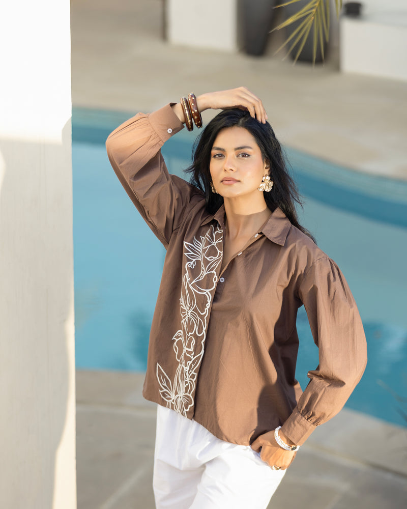 Woman wearing a brown blouse with white embroidery by a pool