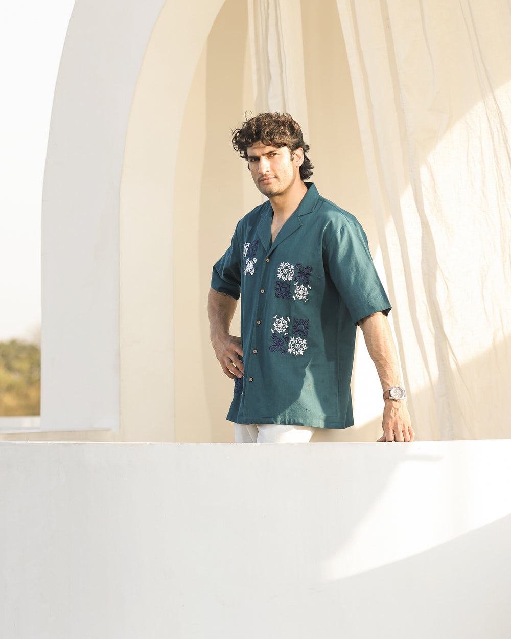 Man wearing a teal shirt with floral patterns standing in front of a white archway.