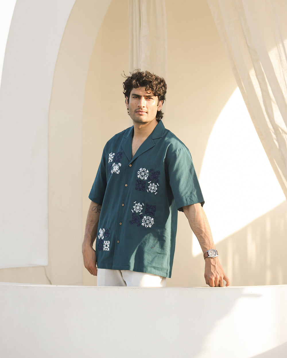 Man wearing a teal shirt with floral patterns standing in front of a white archway.