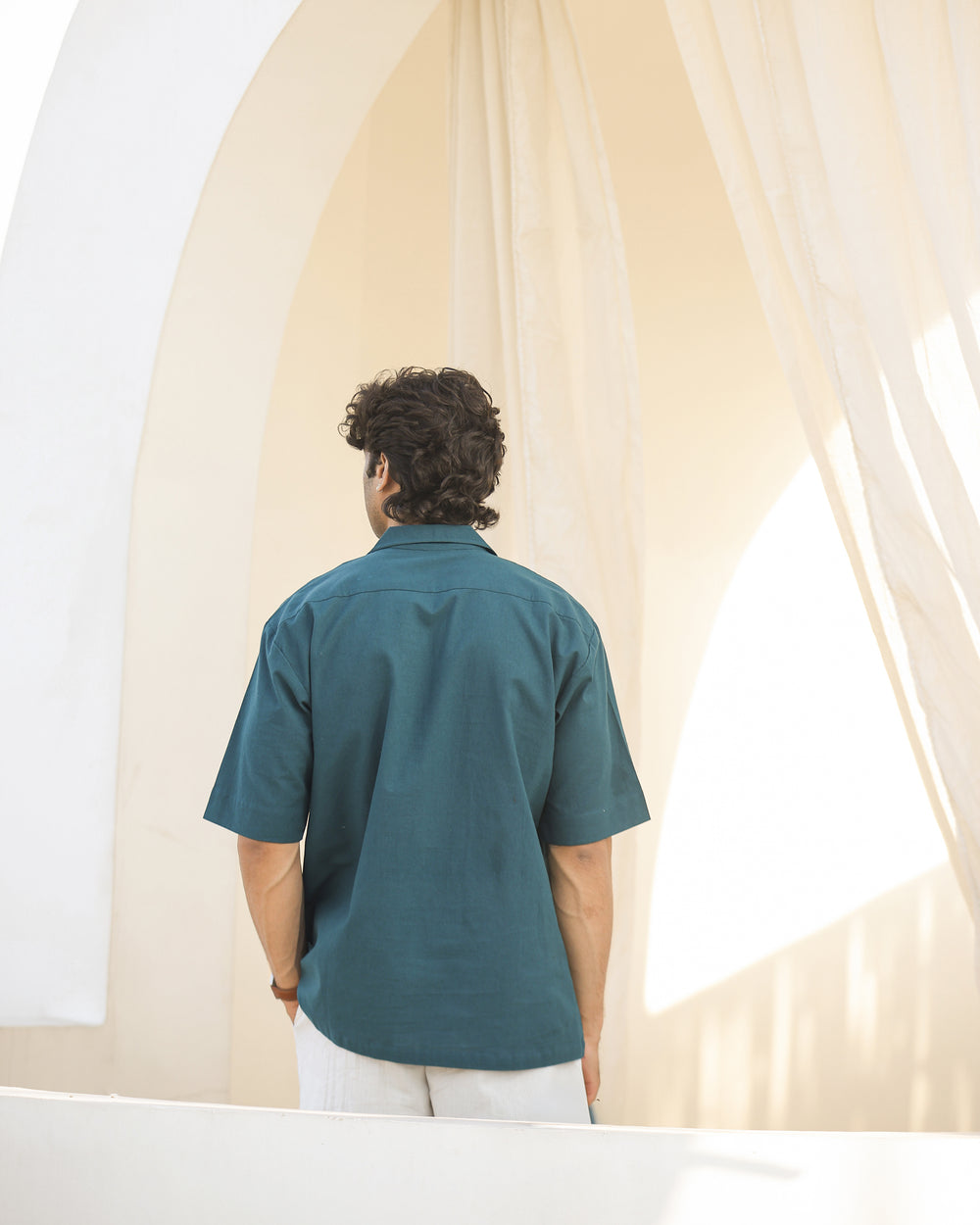 Person wearing a teal shirt standing in front of a curtain