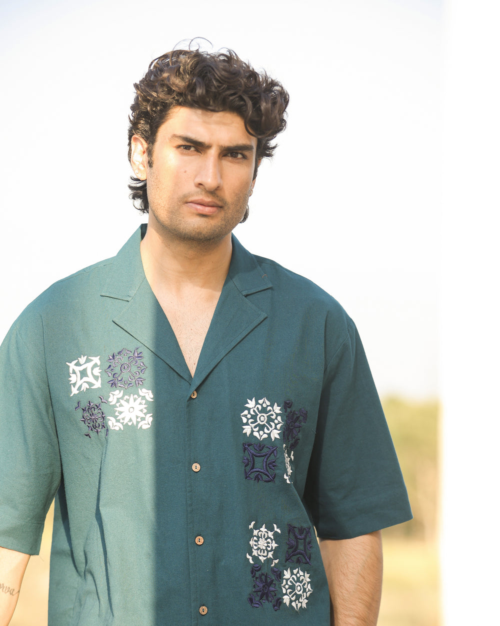 Man wearing a green shirt with floral patterns against a blurred background