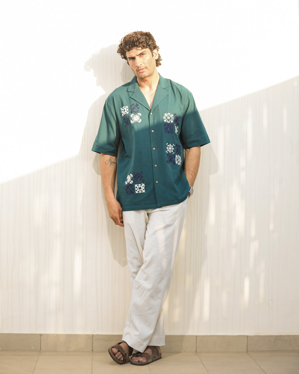 Man wearing a green shirt with floral patterns and white pants against a white background