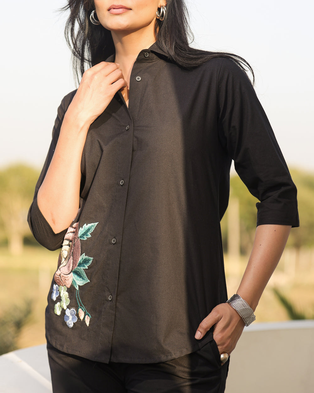 Woman wearing a black shirt with floral embroidery, standing outdoors.