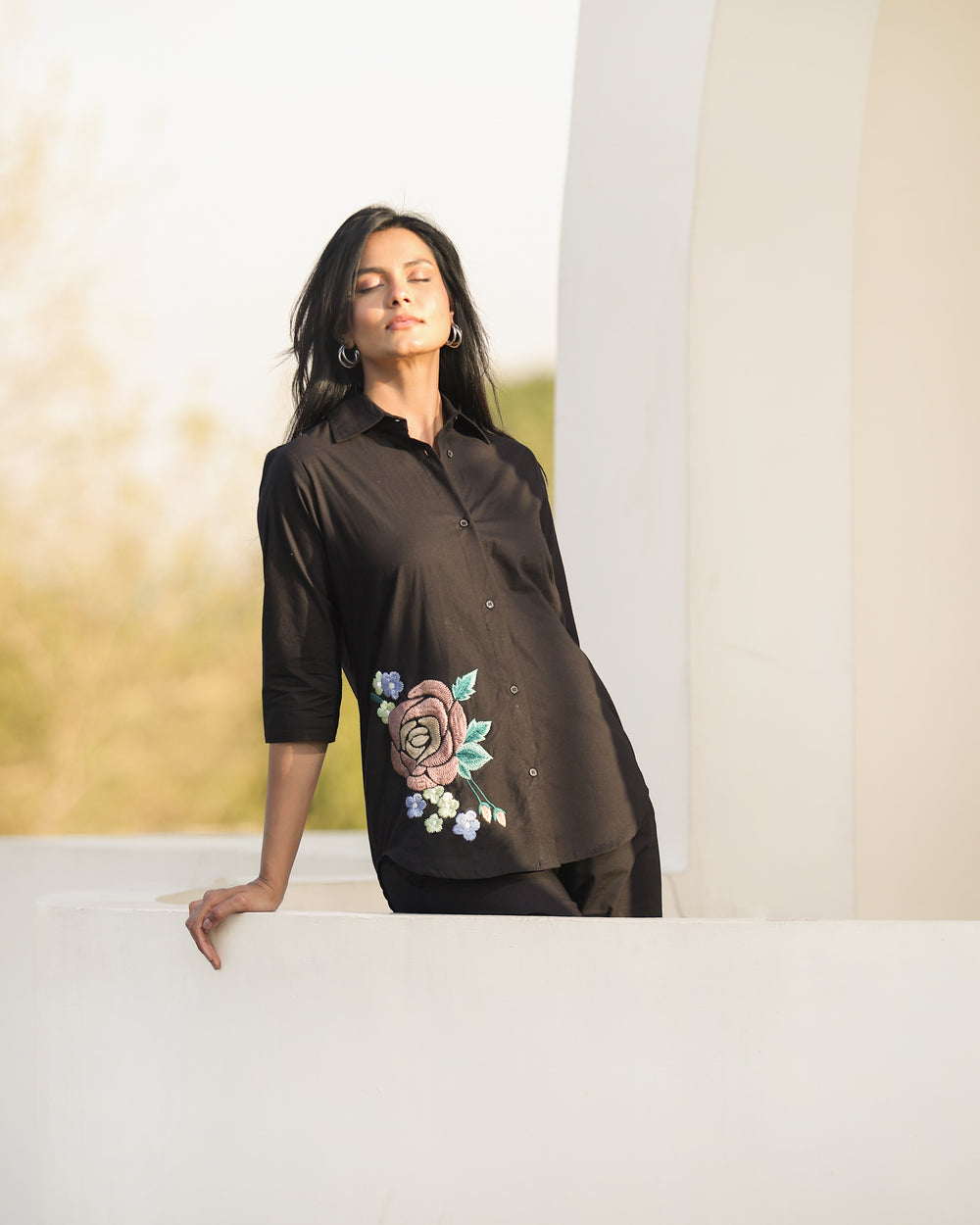 Woman wearing a black blouse with floral embroidery, standing outdoors.