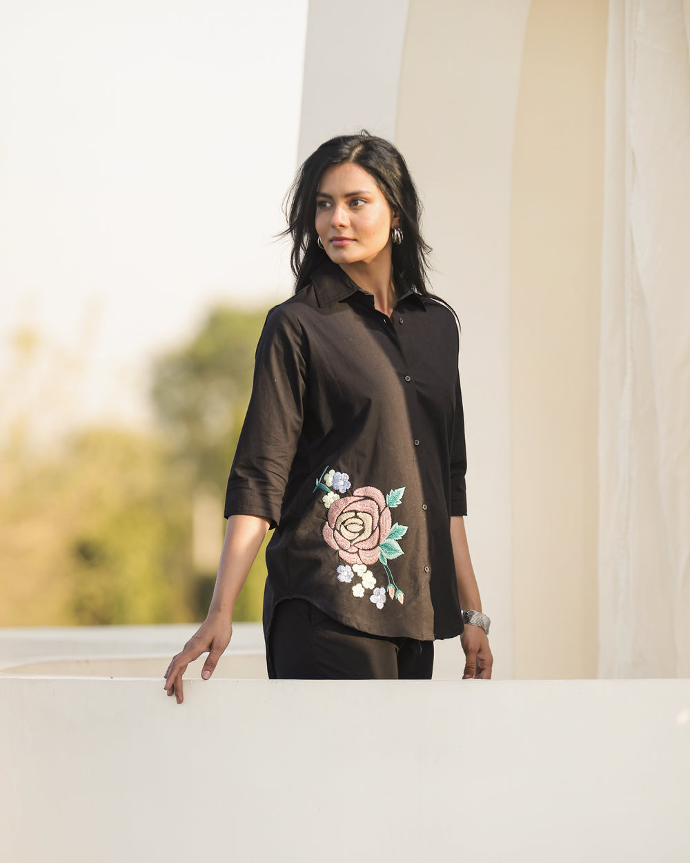 Woman wearing a black shirt with floral embroidery standing outdoors.