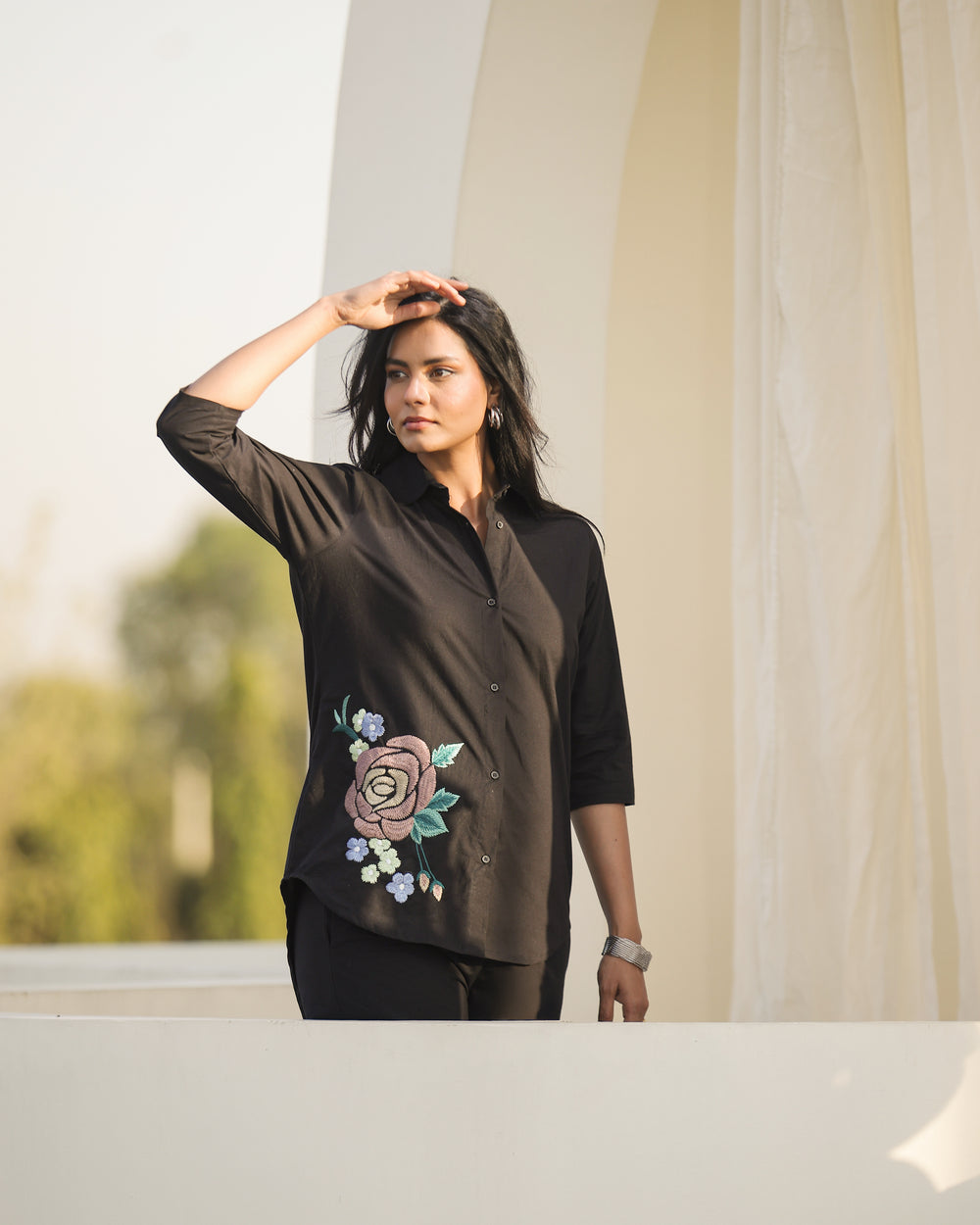 Woman wearing a black blouse with floral embroidery in an outdoor setting